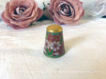 Ancien dé en laiton aux dessins de fleurs en émail cloisonné sur fond bordeaux.