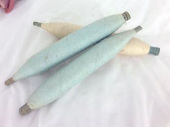 Trio d'anciennes bobines de filature avec fils écru et bleu pastel.