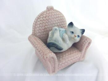 Voici une belle petite figurine en céramique représentant un adorable chaton s'amusant avec une pelote de laine bleue sur un fauteuil en osier rose.
