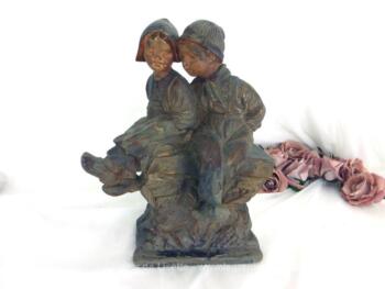 Ancienne statue couple enfants en plâtre polychrome représentant un petit garçon et une petite fille assis sur un rocher.