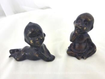 Duo de figurines de bébés en bronze de formes différentes dont le premier est allongé sur le ventre en train de sourire et le deuxième assis avec ses yeux fermés et rond et un doigt dans la bouche.