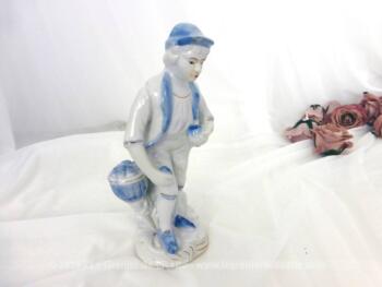 Voici une belle figurine céramique ramasseur de pommes, en blanc et bleu, représentant un homme avec une pomme dans chaque main.