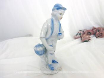 Voici une belle figurine céramique ramasseur de pommes, en blanc et bleu, représentant un homme avec une pomme dans chaque main.