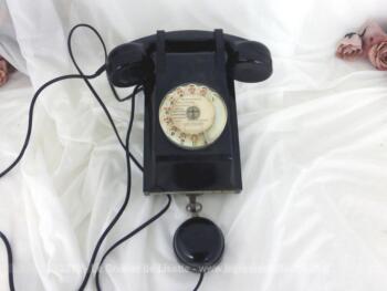Ancien téléphone bakélite mural avec cadran et son écouteur à suspendre. Sur sa plaque métallique dessous, il porte la mention P et T et la date de 1962.