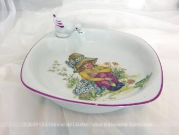 Assiette chauffante bébé porcelaine rétro avec dessin d'une petite fille assise et son bouchon en forme de canard.