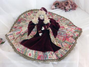 Adorable poupée porcelaine au jupon rond avec tête, bras et jambe en porcelaine. avec une grande robe ample en velours bordeaux habillée de plusieurs volants aux jupons en tulle rose.