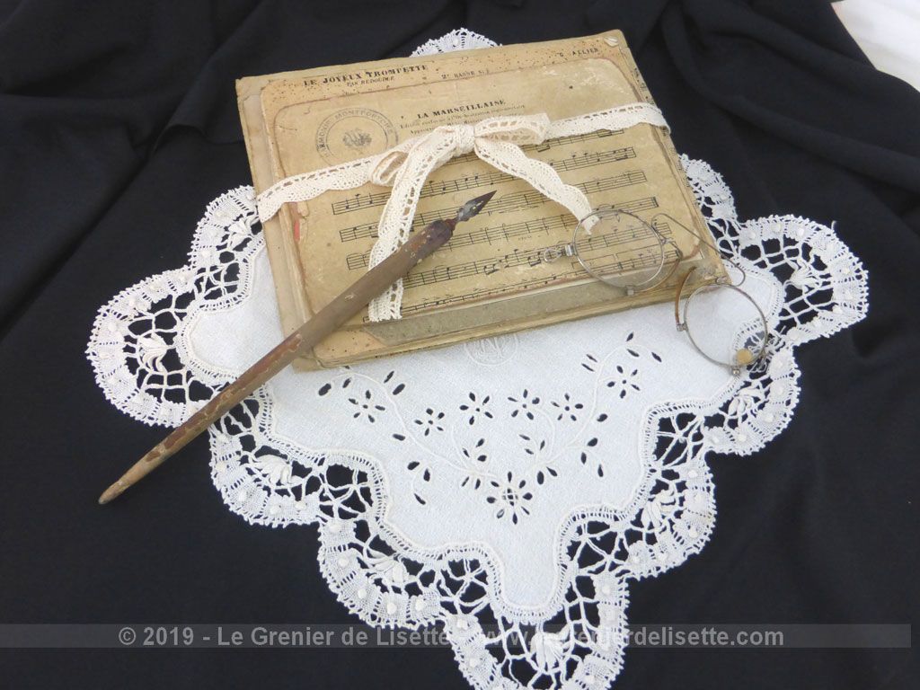 Composition décorative autour de la musique, avec d'anciennes partitions cartonnées, un mouchoir de mariée, un pince nez et un porte plume.