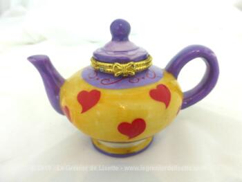 Jolie petite boite à pilules en résine forme de théière avec un beau décor mauve et jaune et petits coeurs rouges, façon "Alice au pays de Merveilles".