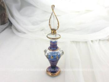 Sur 10 cm de haut, voici un fiole en verre soufflé en forme d'amphore de couleur bleu mauve irisé et décorée de rayures dorées .