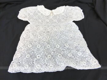 Petite robe fait main au crochet en fil de coton blanc, avec col rond et petites manches courtes, prévue pour fillette ou poupée.