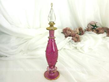Sur 20 cm de haut, voici une fiole rouge en verre soufflé en forme d'amphore et décorée de picots dorés en relief avec son bouchon en forme de feuile.