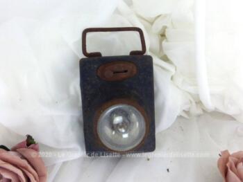 Datant des années 50, voici une ancienne lampe de poche en tôle patinée par les marques d'oxydation avec sur l'avant un bouton poussoir et un verre loupe et bombé pour protéger l'ampoule.