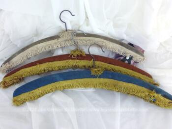 Voici un trio de cintres anciens habillés chacun d'une couleur différente de velours ras et décorés d'un galon frangé.