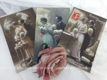 Voici un lot de 3 cartes postales anciennes de couples qui souhaitent "Heureuses Pâques" avec de gros oeufs dans les bras sur des photos colorisées.