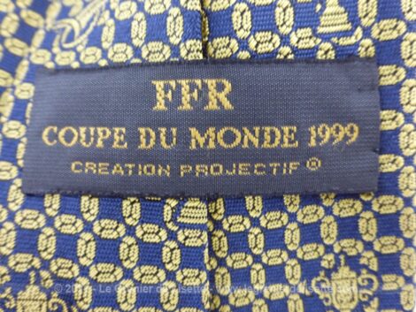 Voici une ancienne cravate en soie portant l'étiquette "FFR Coupe du Monde 1999" et "Création Projectif". Sur fond marine, coupes et ballon se mêlent pour former un motif. Vintage !