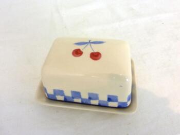 Voici un petit beurrier en céramique en deux parties, avec sur le couvercle un dessin de cerises et une bande de petits carreaux bleu pastel.