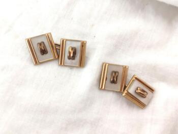 Voici une paire de boutons de manchettes vintages en plaqué or mise en valeur par un décor sur fond de nacre et reliés entre eux par une chainette.