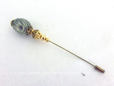 Voici une épingle à chapeaux fibule décorée d'une perle métal tressée avec des décorations dorées et ciselées et son petit embout.
