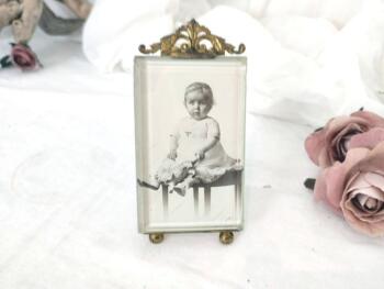 Voici un ancien porte photo en laiton aux décors ouvragés et son verre biseauté avec une photo libre de droit d'un bébé. Pièce unique et superbe !