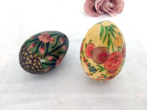 Voici deux œufs en bois décorés, un sur fond jaune paille avec des dessins de fleurs et un sur fond noir avec des fleurs mauves sur tiges !