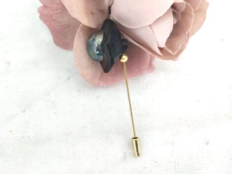 Voici une épingle à chapeaux fibule décorée d'une forme ronde en bakélite aux contours géométriques avec au centre un perle en métal et son petit embout.