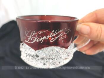 Voici une ancienne tasse de baptême en cristal décorée sur la partie haute d'une laque bordeaux portant la gravure de "Léopoldine 1902".