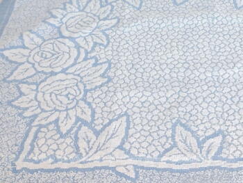 Sur 54 x 80 cm, voici une ancienne serviette de toilette en éponge bleu pastel avec des reliefs blancs dessinant une grande composition de fleurs.