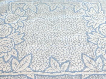 Sur 54 x 80 cm, voici une ancienne serviette de toilette en éponge bleu pastel avec des reliefs blancs dessinant une grande composition de fleurs.