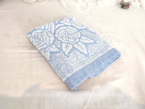 Sur 54 x 80 cm, voici une ancienne serviette de toilette en éponge bleu pastel avec des reliefs blancs dessinant une grande composition de fleurs.