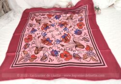 Voici un foulard vintage en crêpe de soie de 72 x 72 cm sur fond bordeaux et rose avec en décors des fleurs rouges aux contours couleur café.