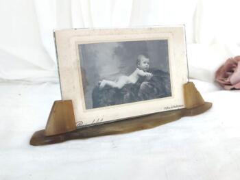 Voici un ancien porte-photo en bakélite avec son verre et sa photo d'un beau bébé nu assis sur son coussin. Pièce unique.