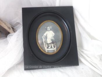 En bois noirci, voici un ancien petit cadre rectangulaire ouvragé pour laisser la place à une photo ovale représentant une petite fille sur une chaise. Pièce unique.