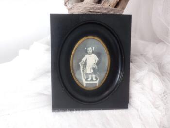 En bois noirci, voici un ancien petit cadre rectangulaire ouvragé pour laisser la place à une photo ovale représentant une petite fille sur une chaise. Pièce unique.