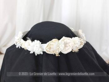 Vintage, voici une couronne-ruban de mariée composée d'un ruban en satin habillé avec des fleurs tissus incrustées de petites perles.