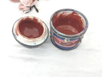 Datant des années 70, voici une ancienne boite marocaine ronde en céramique rose et bleue, habillée par de superbes décors en étain pour un effet shabby. Fait main, elle est estampillée "Safi" et du nom de son créateur.