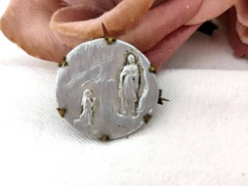 Voici une ancienne broche avec une médaille en fer blanc représentant l'apparition de la Vierge devant Bernadette dans la grotte de Lourdes, le tout sertie dans du laiton sur 1.5 cm de diamètre.