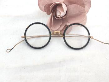 Voici une ancienne paire de lunettes rondes au contour en bakélite imitation écaille de tortue avec des branches qui se terminent par une boucle. Vraiment vintage !