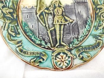 Superbe assiette de collection en barbotine aux tons pastel à l'effigie de Jeanne d'Arc portant sur le pourtour les mentions Gloire, Honneur, Liberté, Patrie. 