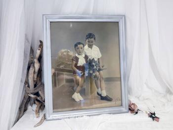 Sur 56.5 x 46.5 x 2 cm, voici un cadre en bois, peint couleur vieil argent  mettant en valeur une photos représentant deux garçonnets et signée par le photographe. Tout dans ce cadre nous transporte avec nostalgie dans le monde vintage des années 50!