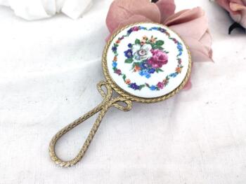 Adorable miroir biseauté face à main en laiton bien ouvragé avec en décoration un écusson rond en porcelaine décoré d'un beau bouquet de fleurs fuchsia.