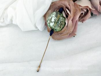 Voici une épingle à chapeaux fibule avec en décoration une grande pastille de verre vert pale avec des incrustations irisées avec une perle de verre bordeaux fait main bordeaux au dessus et une en dessous. Petit embout à l'extrémité.