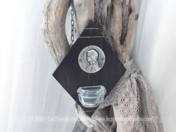 Voici un bénitier original en bois en forme de losange avec une médaille en métal à l'effigie de la Vierge Marie et un petit réceptacle en verre avec une chaine pour suspendre.