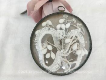 Un adorable petit cadre rond en laitons avec une vitre en plexiglas bombé mettant en valeur des fleurs en cire, vestiges d'une couronne de mariée.