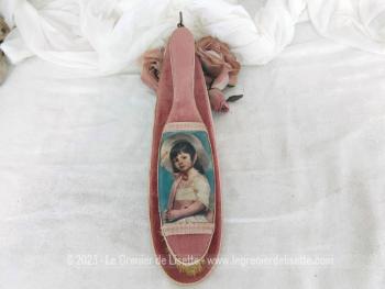 Datant des années 60, voici une brosse à habits vintage avec au dos une incrustation en soie d'un dessin d'une petite fille modèle, le tout posé sur son support mural en velours vieux rose.