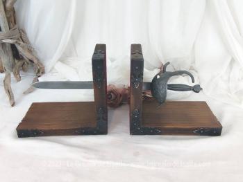 Voici deux serre-livres en bois habillé par des ferrures noire et décoré chacun d'une partie d'une épée pour donner un effet traversant aux livres exposés
