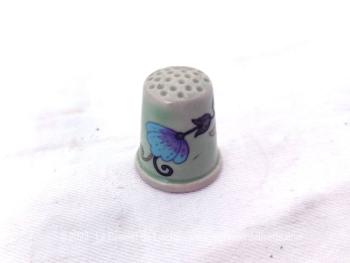 Beau dé à coudre en céramique décoré d'une guirlande fleurie dans des tons pastel, peinte à la main, le tout sur fond bleu pâle.