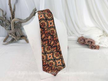 Voici une superbe cravate vintage seventeen, décorée de motifs d'arabesques psychédéliques dans les tons orangés et chocolat portant l'étiquette "Tergal et Fibre Polyester".