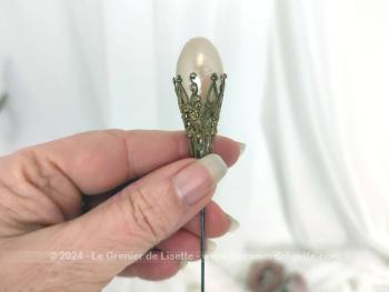 Voici une ancienne épingle à chapeaux avec une grande perle nacrée sertie dans un long habillage en laiton ciselé en volutes et arabesques l pour la décorer comme un bijoux. Top vintage.