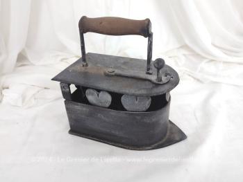 Voici un ancien fer à repasser en fonte patiné en noir avec réservoir à braises et décoré de coeurs muni d'un couvercle, de son systeme de fermeture et de son manche en bois.