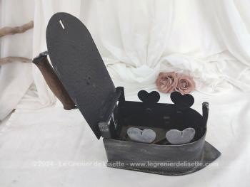 Voici un ancien fer à repasser en fonte patiné en noir avec réservoir à braises et décoré de coeurs muni d'un couvercle, de son systeme de fermeture et de son manche en bois.